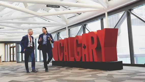 Two men chatting as they walk in front of a 3D Calgary sign at the Calgary TELUS Convention Centre