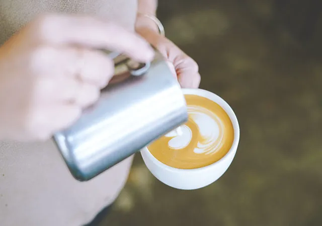 barista pouring milk into an espresso drink to make latte art at Monogram