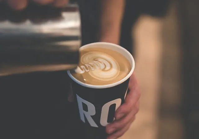barista pouring milk into a coffee to go to make latte art at Rosso