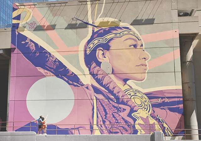couple admires large mural 'SÔHKÂTISIWIN' by Kevin Ledo in downtown Calgary