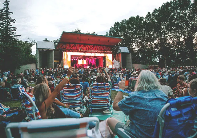 crowd seating on blankets and in lawn chairs enjoying live music onstage during Calgary Folk Fest