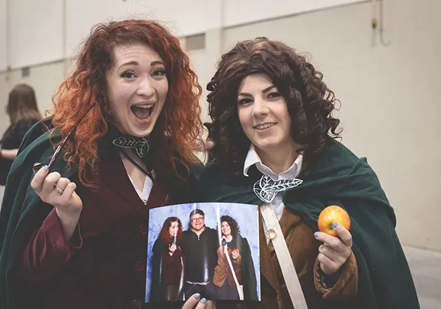 two girls dressed in LOTR cosplay showing off a photo of themselves with Sean Astin