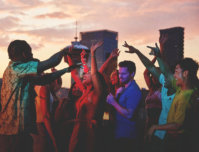 group of friends dancing on an outdoor rooftop with the Calgary skyline in the background