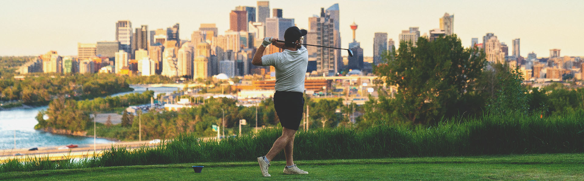 golfer taking a swing at Shaganappi Point Golf Course with the skyline in the background