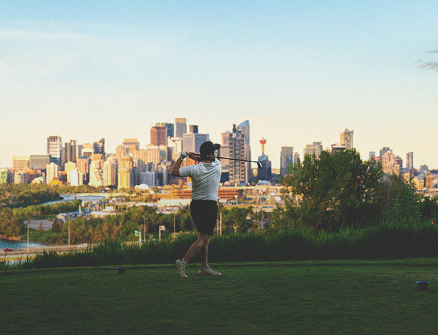 golfer taking a swing at Shaganappi Point Golf Course with the skyline in the background