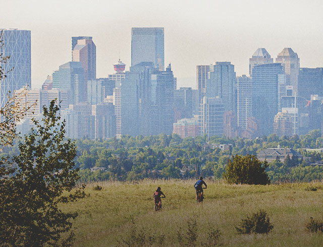 cyclists biking through Nose Hill Park with the Calgary skyline in the background