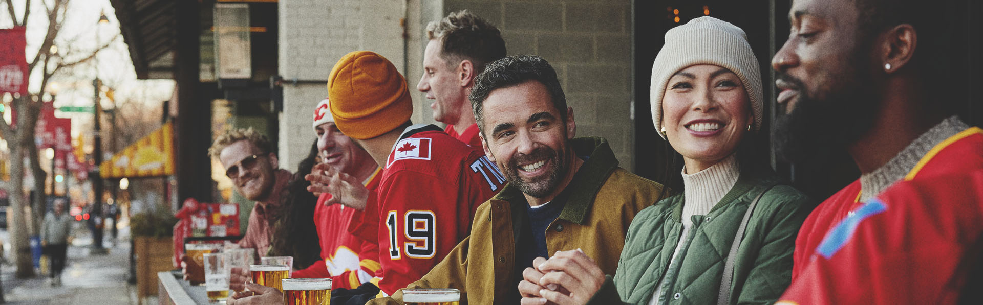 group of friends in warm clothes and hockey sweaters sitting enjoying pints outside before a Flames hockey game a Trolley 5