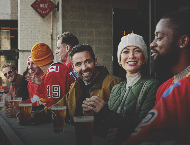 group of friends in warm clothes and hockey sweaters sitting enjoying pints outside before a Flames hockey game a Trolley 5