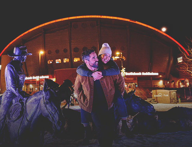 couple are smiling in front of Scotiabank Saddledome