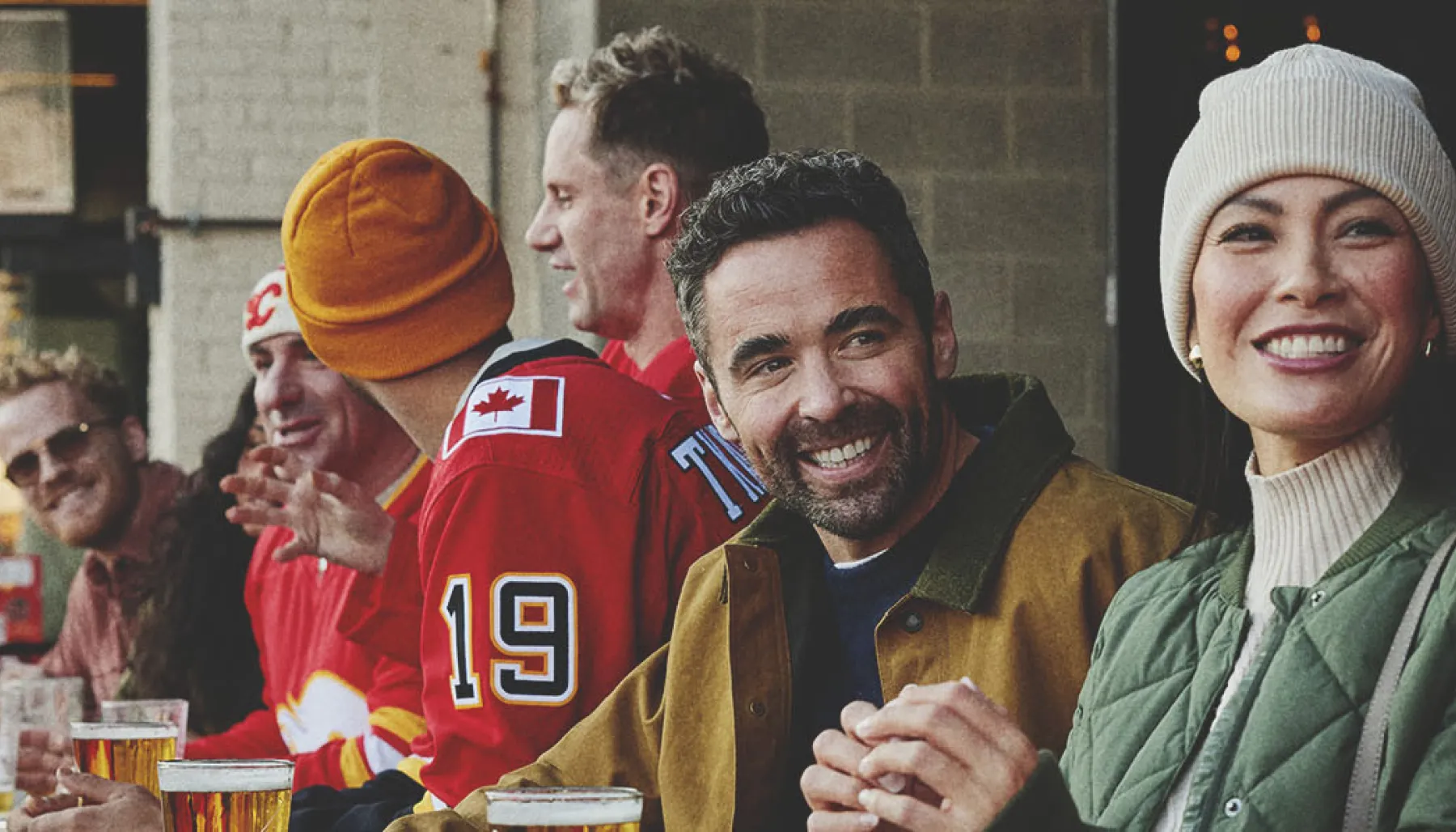 group of friends in warm clothes and hockey sweaters sitting enjoying pints outside before a Flames hockey game a Trolley 5