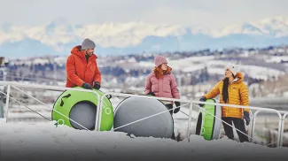 family at WinSport's Servus Tube Park with mountains in the background