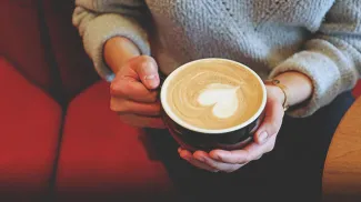woman holding a coffee with latte art in the shape of a heart at Deville Coffee