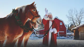 Santa stands with two harnessed horses at Heritage Park waving to someone off camera
