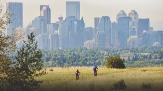 cyclists biking through Nose Hill Park with the Calgary skyline in the background