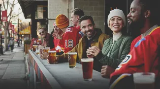 group of friends in warm clothes and hockey sweaters sitting enjoying pints outside before a Flames hockey game a Trolley 5