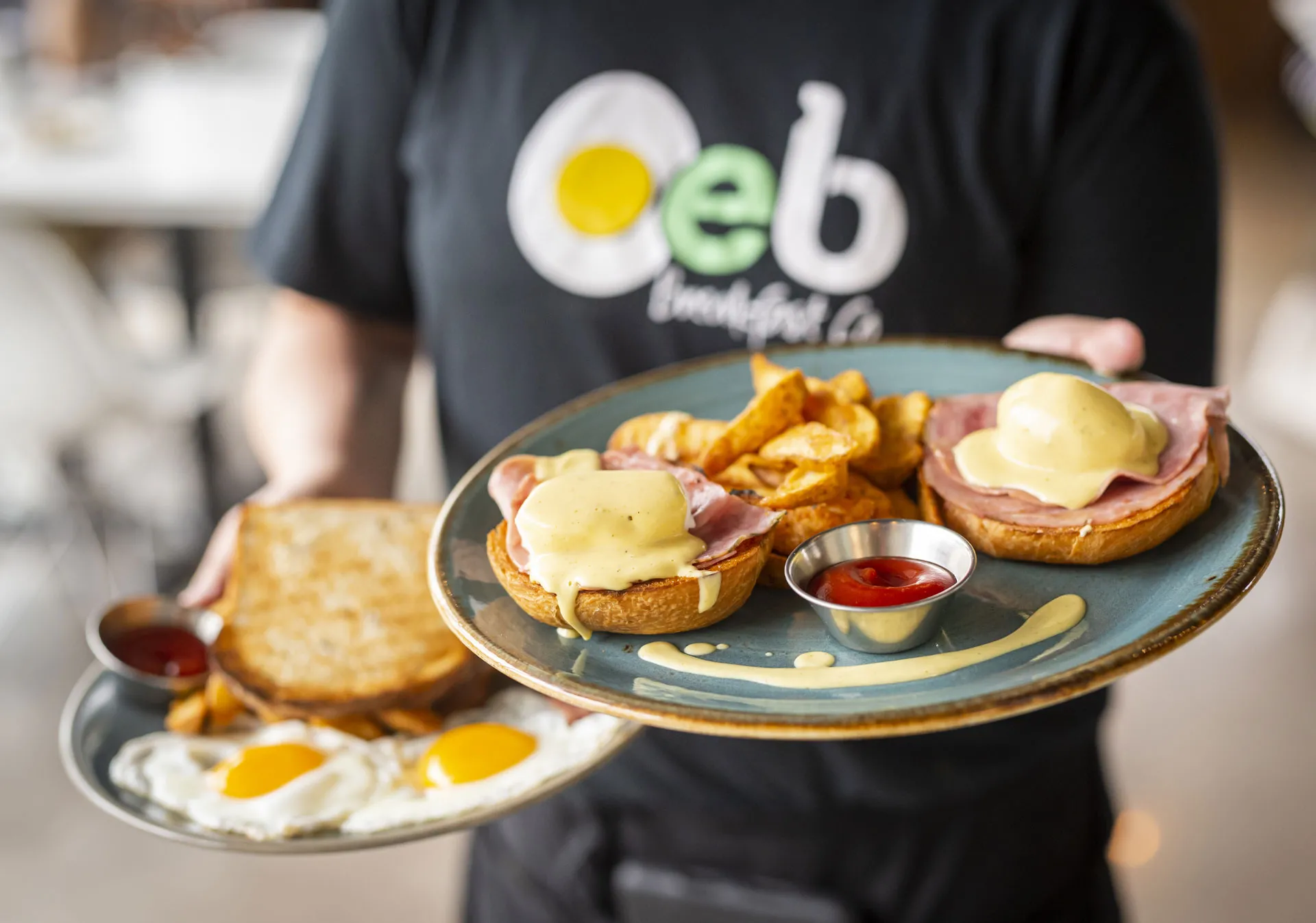 A server bringing a table eggs benedict at OEB Breakfast Co.