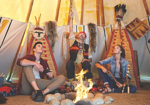 Three people sit in a tipi in front of a fire to listen to indigenous storytelling