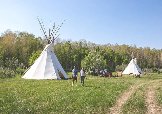 Couple walks outdoors along a row of tipi's at Blackfoot Crossing