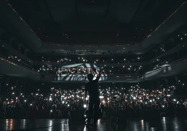 performer onstage facing the crowd holding up cell phone lights at Jack Singer Concert Hall