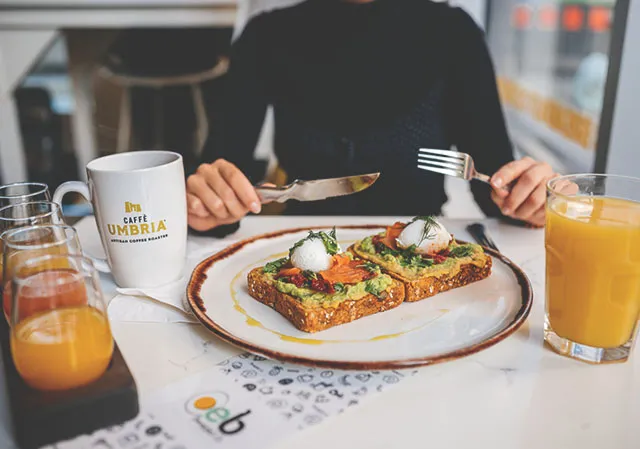 woman sits at a table with a plate of breakfast and a mimosa sampler