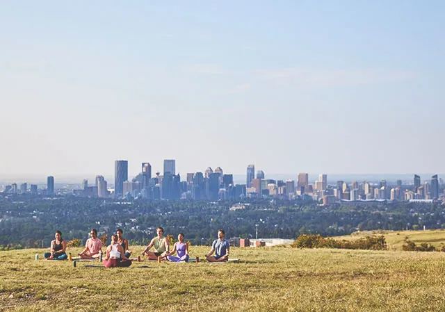group practices yoga in Nose Hill Park with the Calgary skyline in the background