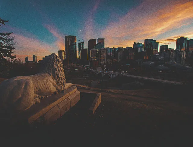 downtown Calgary skyline during a colourful sunset seen from Rotary Park facing south down Centre street, with the Centre Street stone lion in the foreground
