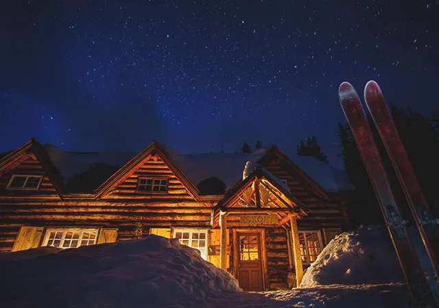 Exterior of Skoki Lodge in winter with starry skies and skies stuck up in the snow in the foreground