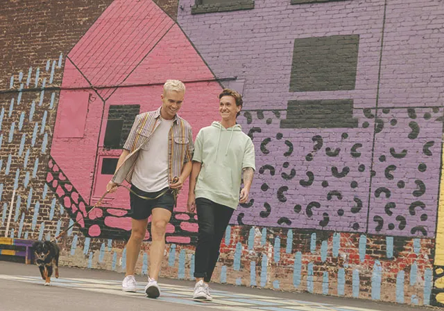 couple walking their dog through downtown Calgary with a public art mural behind them