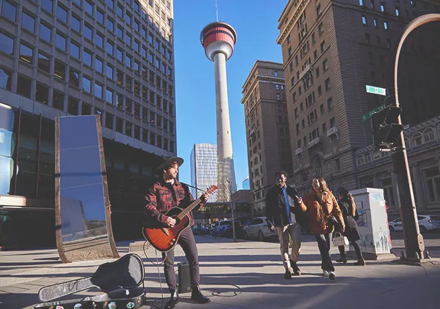 two people stop to listen to a street performer in downtown Calgary with the Calgary Tower directly behind them