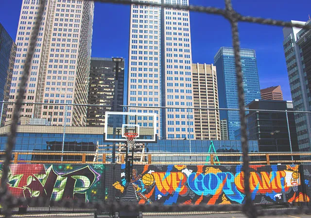 a basketball hoop and graffiti can be seen amongst sky scrapers at Calgary's High Park