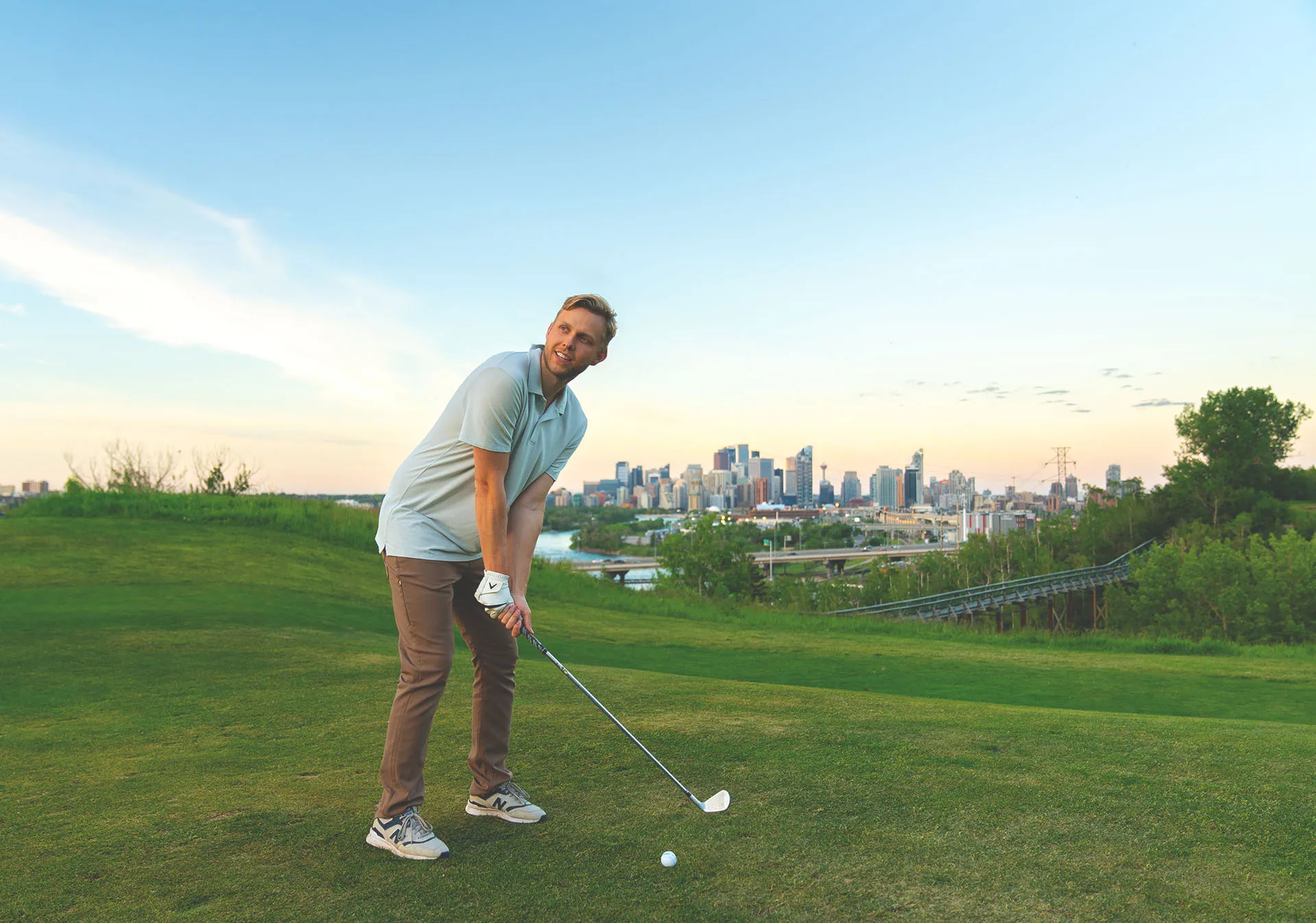 golfer taking a swing at Shaganappi Golf Course with the skyline in the background