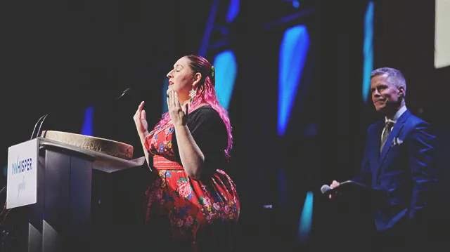 a woman speaking at a podium on stage at Calgary TELUS Convention Centre